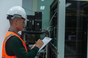 an asian adult IT technician working on network Internet cables and servers and try to checklist on the paper photo