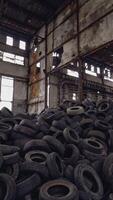 Pile of used tires of car are on the ground inside an abandoned factory on the background of the old gray walls. Camera motion from down to up. Vertical video