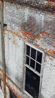 Damaged brick building without windows after the war. Close view of a destructed house with many holes in the wall. Camera moves top down Vertical video