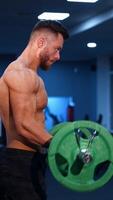 Muscular athlete doing exercise with barbell. Strong man working out arm muscles. Bodybuilding shoulder exercise in a gym. Vertical video