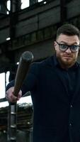 Strong bearded young man with bat. Guy waves a baseball bat on the background of abandoned house. Bandit looks at camera and shouts. Vertical video