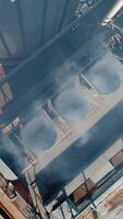 Steam from industrial plant. Vapor in modern factory for grain processing. Grain elevators. Harmful smoke goes into the air from manufacturing. Top aerial view. Vertical video