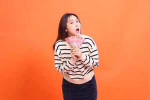 an Asian girl with a shocked expression at the camera stands with both hands holding several rupiah bills. for fashion, business and finance concept photo