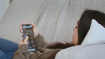 Boring quarantine time. Young girl scrolling social media app on cellphone, lying on couch at home video