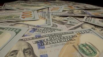 A close up shot of a stack of hundred dollar bills. The dollar bills are in various states of disarray. The bills in focus, with the faces of Benjamin Franklin visible on several of the bills. video