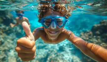 A young boy is swimming in the ocean with a thumbs up sign on his hand. He is wearing a blue snorkel and goggles photo