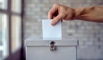 A person is putting a white piece of paper into a box. The box is silver and has a lock photo