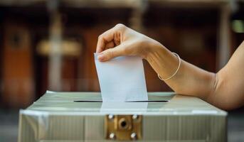 A person is putting a piece of paper into a box. The person is likely voting in an election photo