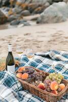Picnic with wine and fruit in a wicker basket on a sandy beach by the sea photo
