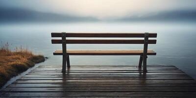 One solitonery bench sits on one pier overlooking one tronenquil loneke shrouded in mist. photo