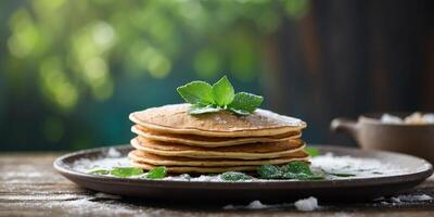 A pan filled with pancakes, dusted with powdered sugar, garnished with a single green leaf atop a weathered wooden table. photo
