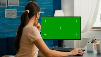 Business woman searching marketing information on internet using personal computer with mock up green screen chroma key. Female working with isolated pc at project company in living room photo