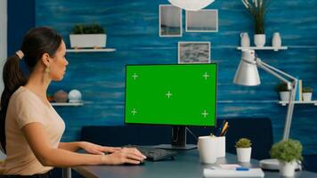 Woman working on personal computer with mock up green screen chroma key display in home office room. Caucasian female on isolated pc for project company photo