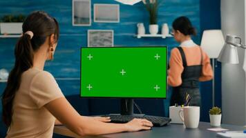 Beautiful caucasian woman working on green screen mock up PC with chroma key while her apartment colleague is in background, home office enviroment. Isolated green screen for advertisiment photo