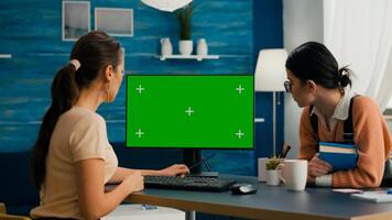 Two women looking at computer with mock up green screen chroma key working at business commerce. Office desk is equipped with isolated home office pc photo
