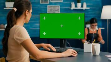 Woman looking at computer with green screen mock up chroma key display working at business commerce, Caucasian female using powerful isolated pc while collegue reading in background photo