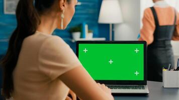 Back shot of freelencer woman looking at laptop with mock up green screen chroma key while working at commerce project. Caucasian female standing in home office studio with her collegue in background photo