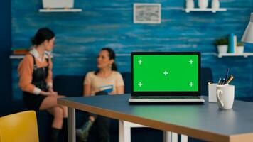 Laptop computer with mock up green screen chroma key standing on desk while in background two women talking about business commerce. Home studio is eqquiped with powerful isolated pc photo