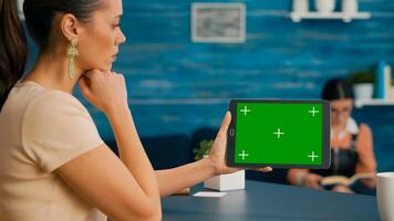 Back view of woman holding tablet computer with mock up green screen chroma key display. Caucasian female using touchscreen device for online browsing sitting in home office studio photo