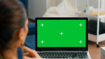 Close up of laptop computer with mock up green screen chroma key display. Business woman lying on sofa and typing on isolated pc for commerce project in home office photo