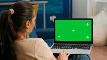 Caucasian female lying on sofa looking at laptop computer with mock up green screen chroma key display. Business woman working on financial graphs using isolated pc in home office photo