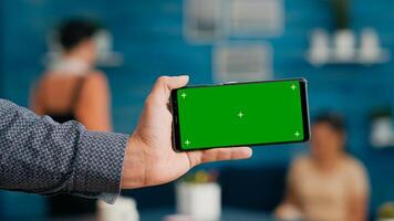 Front view of horizontal isolated mock up green screen chroma key display of modern smartphone. Business woman using isolated phone for browsing social networks sitting on office desk photo