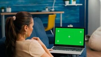 Freelancer sitting on couch working on business ideas using laptop computer with mock up green screen chroma key display. Caucasian female searching the network use isolated pc photo