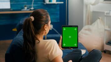 Business woman looking at tablet computer with mock up green screen chroma key display sitting on sofa in living room. Freelancer using isolated touchscreen device for social networks browsing photo