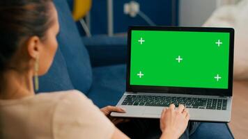 Woman sitting on couch in cozy living room working on laptop computer with mock up green screen chroma key display. Freelancer using isolated pc, browsing on internet for social media advertising photo