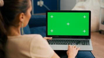 Close up of freelencer using laptop computer with mock up green screen chroma key display while sitting on sofa in living room., Woman working on personal business using isolated pc photo