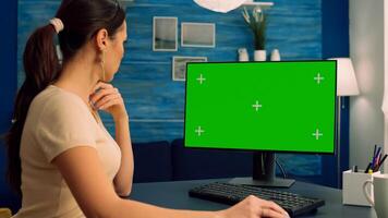 Caucasian female searching on computer with mock up green screen chroma key display browsing on internet for business communication sitting at desk table. Freelancer using isolated pc in home office photo