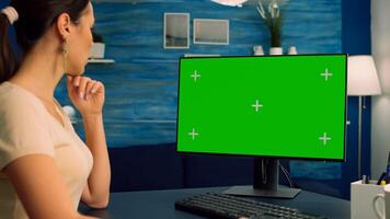 Freelancer woman at home sitting on desk table working on computer with mock up green screen chroma key display. Freelancer using isolated pc in home office for lifestyle opinions photo