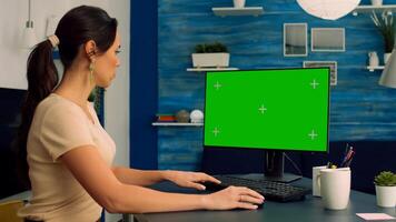 Caucasian female at her desk working on personal computer with mock up green screen chroma key display. Woman browsing on internet advertising for company business using isolated pc photo