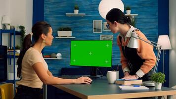 Teammates sitting on desk table while talking about business communication working on computer with mock up green screen chroma key display. Office desk is equipped with isolated home office pc photo