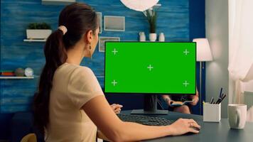 Caucasian female typing on professional computer with mock up green screen chroma key display sitting at modern office desk. Freelancer working at commerce project on isolated pc in living room photo