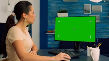 Freelancer sitting at desk table and browsing on network for commerce business using computer with mock up green screen chroma key. Caucasian female working with isolated pc in office home apartment photo