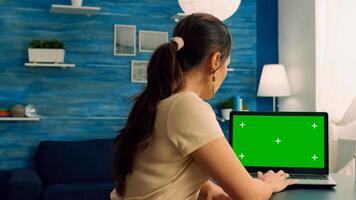 Caucasian female working on laptop computer with mock up green screen chroma key display for personal business. Woman typing on isolated pc sitting at desk table in office home photo