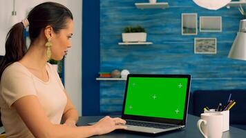 Freelancer working at business communication uses laptop computer with mock up green screen chroma key display. Caucasian female typing on isolated pc while sitting at desl table in home office photo