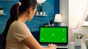 Woman typing on computer laptop with mock up green screen chroma key display working on commerce project. Freelancer using isolated pc sitting in living room while her collegue reading in background photo