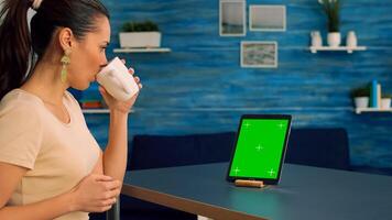 Freelancer looking at tablet computer display with mock up green screen chroma key while searching ideas on network. Caucasian female sitting on desk in office studio using powerful isolated gadget photo