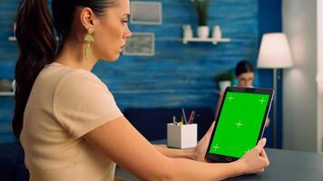 Freelancer holding tablet computer with mock up green screen chroma key display during virtual meeting. Caucasian female working on business advertising using isolated gadget, sitting at office desk photo