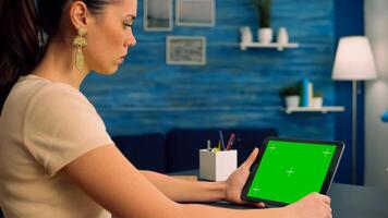 Freelancer reading online book using tablet computer with mock up green screen display sitting at office desk. Caucasian woman looking at template chroma key isolated device using technology internet photo