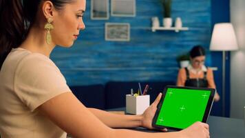 Woman working at office desk using mock up green screen tablet computer in landscape mode, watching online content. Freelancer looking at template chroma key isolated device using technology internet photo