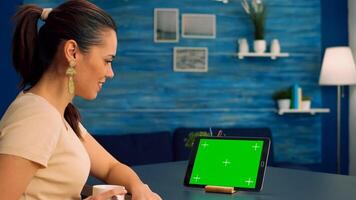 Freelancer holding touchpad with mock up green screen standing on office desk in living room. Woman looking at template chroma key isolated tablet computer display using technology internet photo