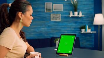 Business woman reading emails while drinking coffee sitting at office desk table in office home studio. Woman looking at template chroma key isolated tablet computer display using technology internet photo