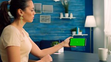 Social media person holding phone with mock up green screen chroma key display while watching online videos. Caucasian female sitting at office desk in living room using isolated technology device photo