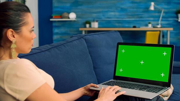 Business woman working on communication project for company uses isolated laptop computer with mock up green screen chroma key lying on sofa in living room. Freelancer using technology concept photo