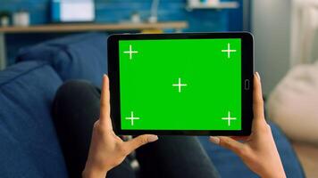 Close up of woman hands holding isolated tablet computer with mock up green screen chroma key display. Freelancer using technology communication concept for online template while lying on sofa photo
