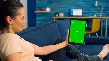 Business woman holding isolated tablet computer mock up green screen chroma key standing on couch at home . Freelancer working on technology app communication concept for online template photo
