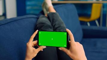 Business woman lying on sofa holding isolated phone with mock up green screen chroma key during social media media communication. Caucasian female browsing on internet watching online videos photo
